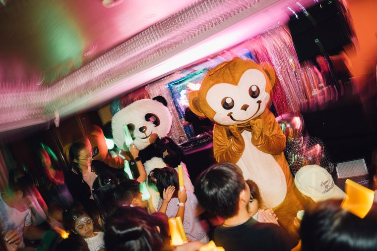 Monkey and panda mascots meeting children under pink party lights