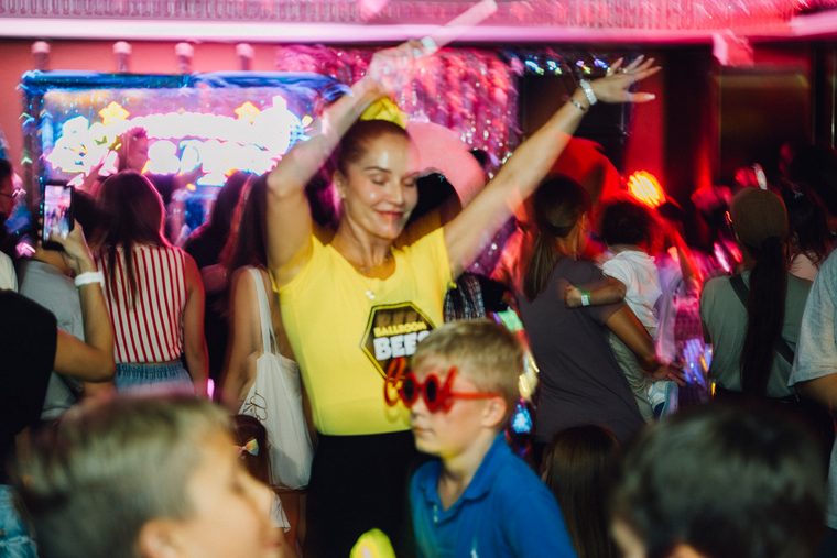 A woman in yellow and a child raising their hands on the dance floor